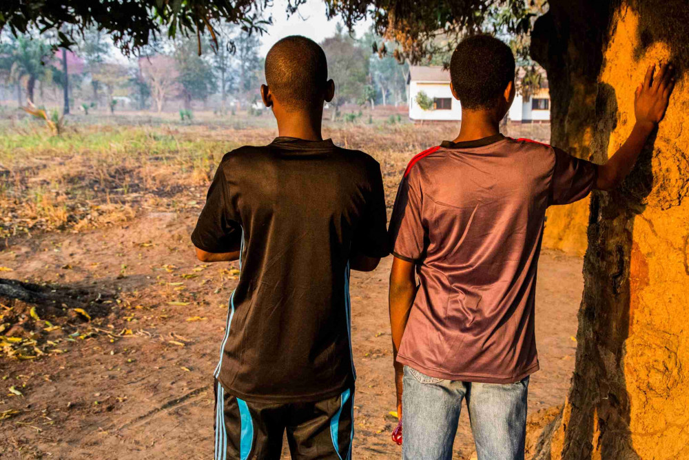 Two young men in CAR standing next to a tree looking into the distance